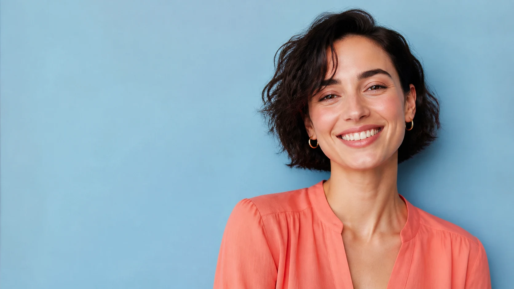 A polished beauty portrait of a woman in a coral blouse against a sky-blue wall